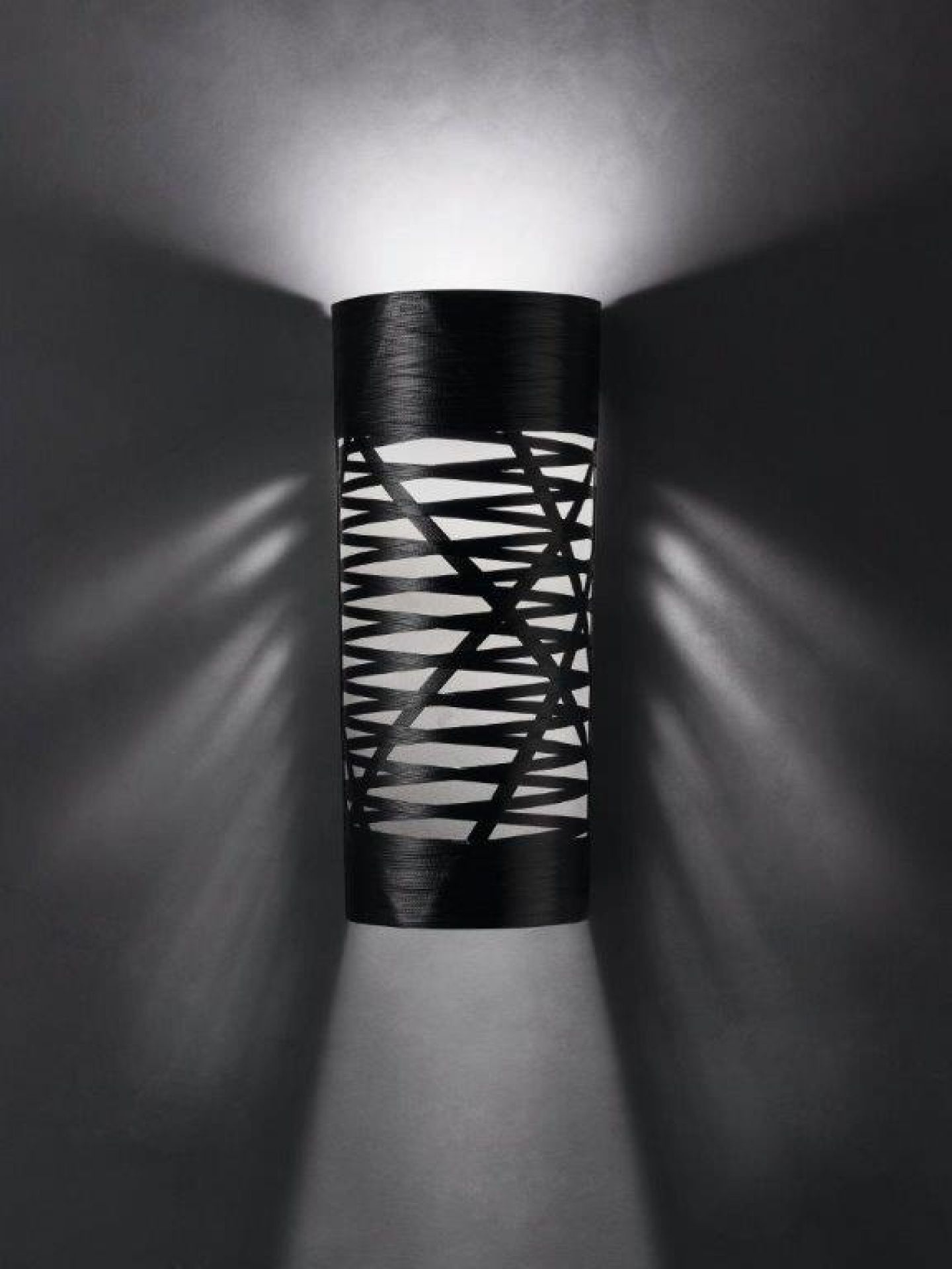 Schwarze Tress Wandleuchte von Foscarini mit zylindrischem Design und dekorativen Lichteffekten an einer dunklen Wand.